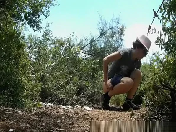Woman with hat pulls pee in middle of bushes
